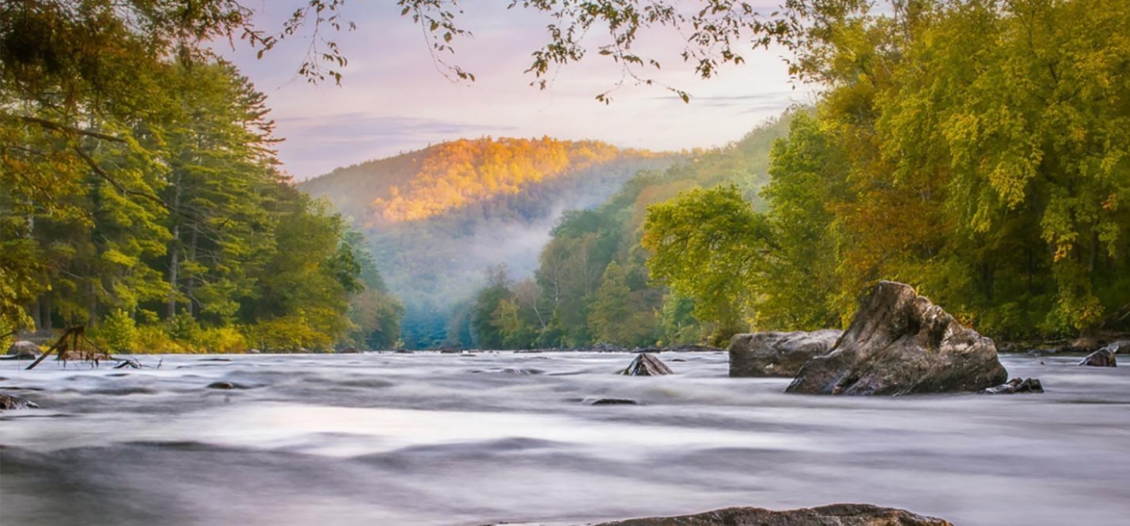 View of river with rocks and trees and mountains in the background (Instagram@janehaslamphotography_nature)
