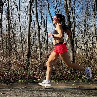 A woman running on path with woods behind (Instagram@mazyruns)