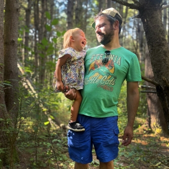 A man holding a laughing child in a beautiful forest.