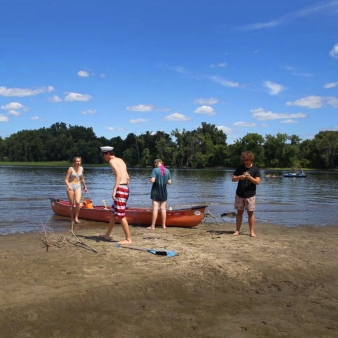 A group of people on the beach with a canoe, enjoying the sun and the water.