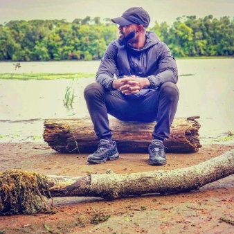 A man sitting on a log , waterside.
