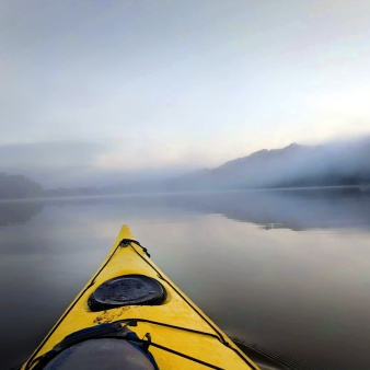 A serene river with a kayak gliding through calm waters, surrounded by a misty fog.