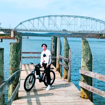 A man standing on a dock with his bike, enjoying the view of the water.
