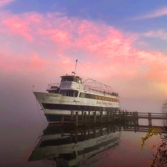 A boat docked on misty water beneath a pink sky.