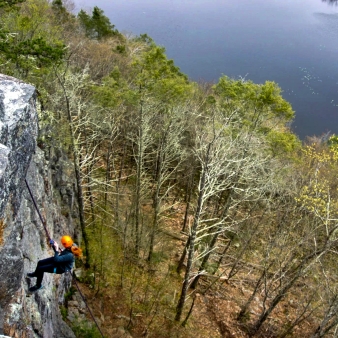 A climber scaling a rock face overlooking a serene pond.