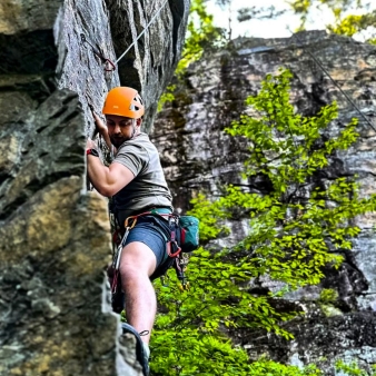 A man scaling a rock wall in the forest.