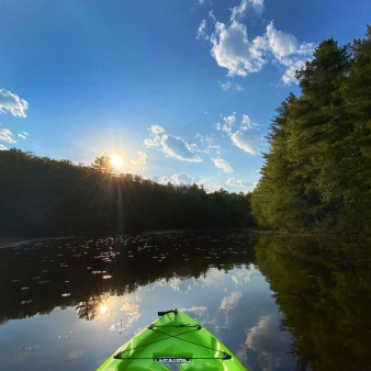 A serene sunset with a kayak gliding on the calm water.